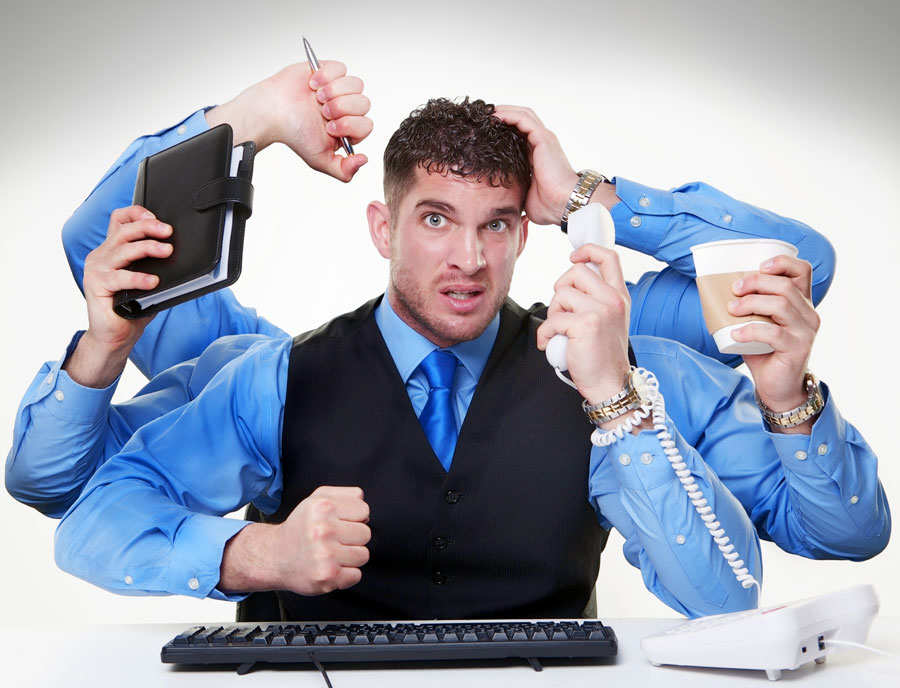 Frustrated office worker portrayed with multiple arms, symbolizing multitasking stress, holding a notepad, pen, phone, coffee cup, and punching fist, representing the chaos of managing ISO 9001 certification before using Safety PAL Software.